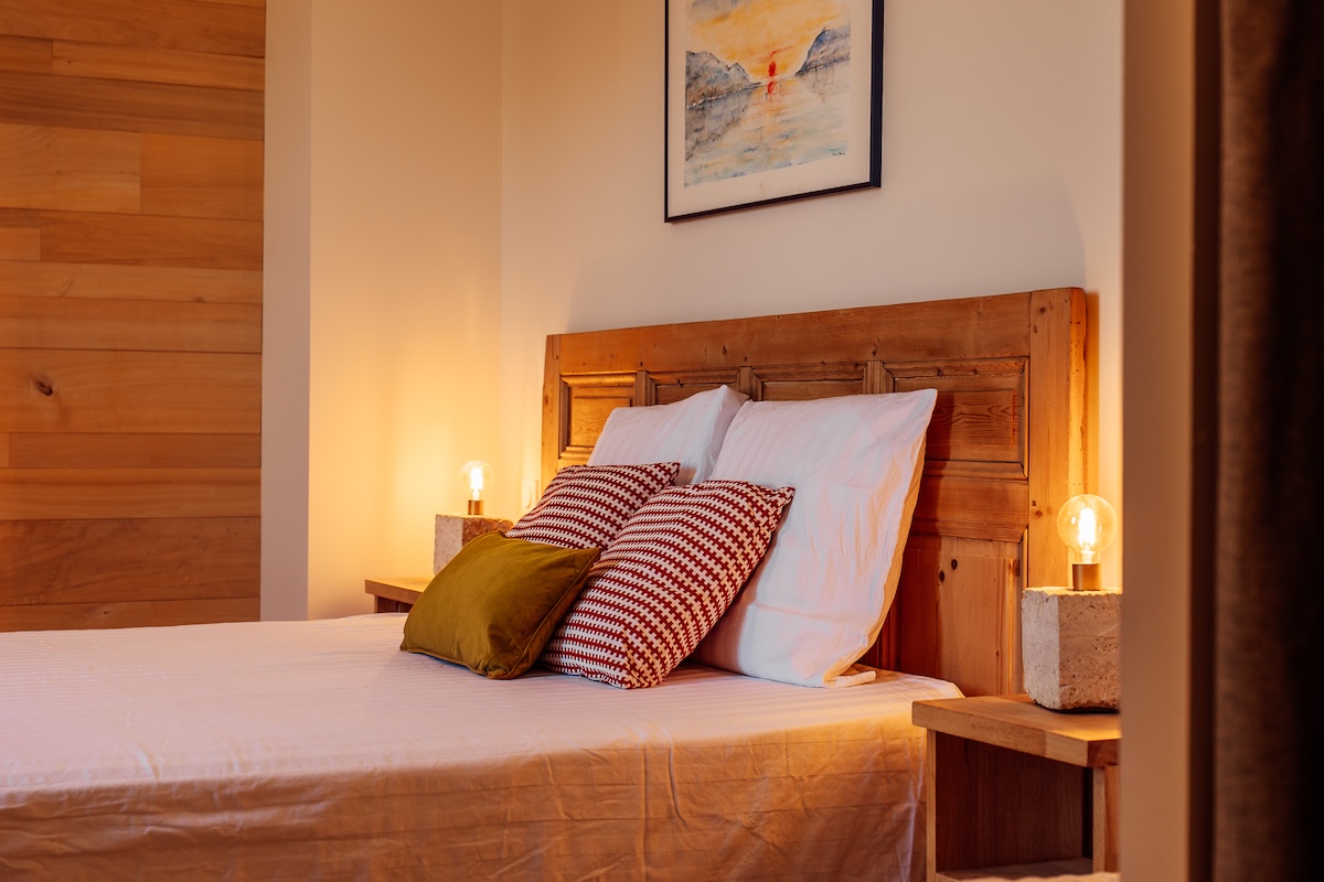 La tête de lit en bois avec sa talle de nuit en bois et jute, sa lampe en pierre, des coussins en velours, une ambiance très cosy pour la chambre duo