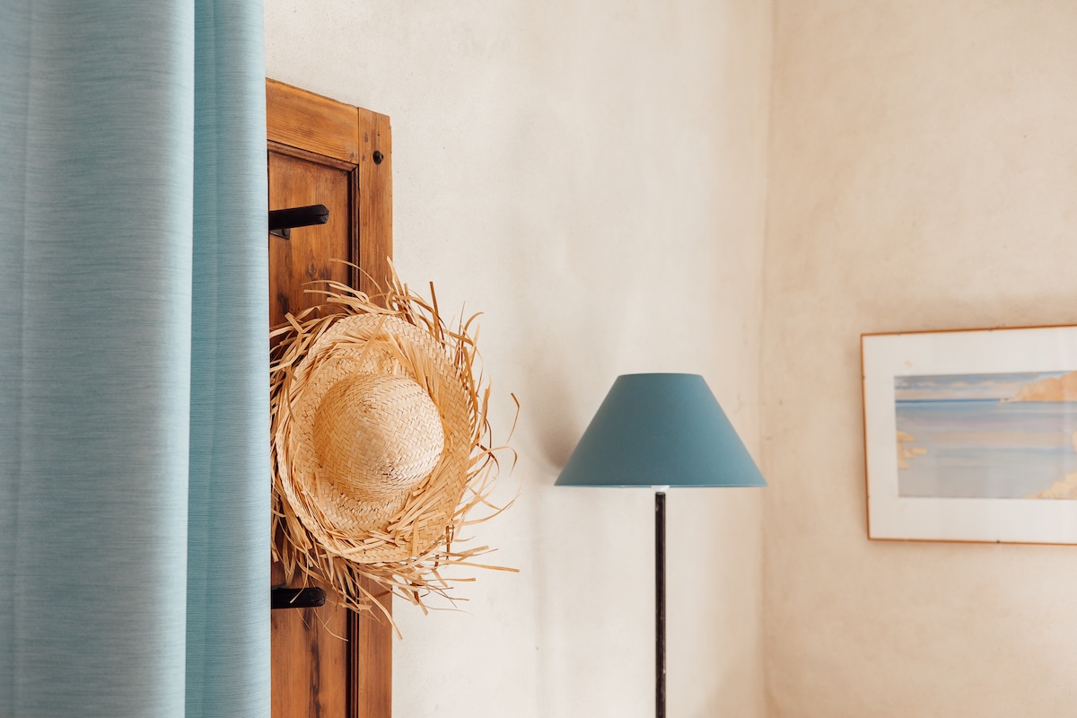 Un lampe bleue, un cadre d'une peinture à l'aquarelle, des jolis rideaux bleu et un porte manteau fait maison, la décoration du gîte